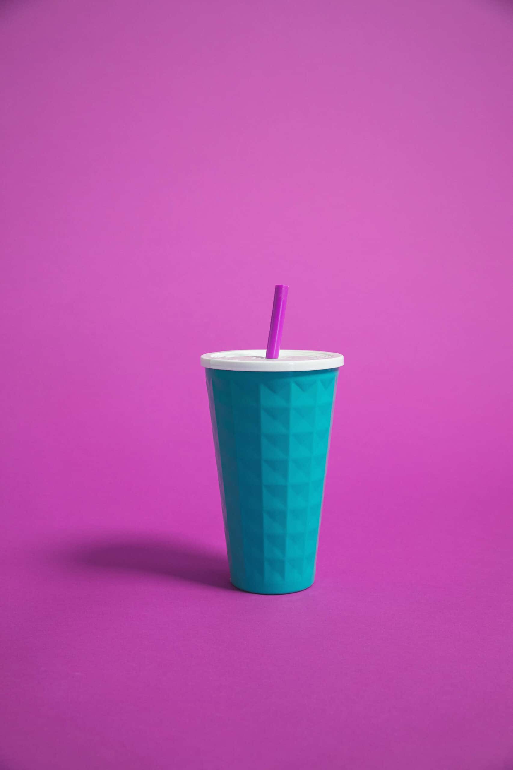 Blue cup with straw against a purple background.