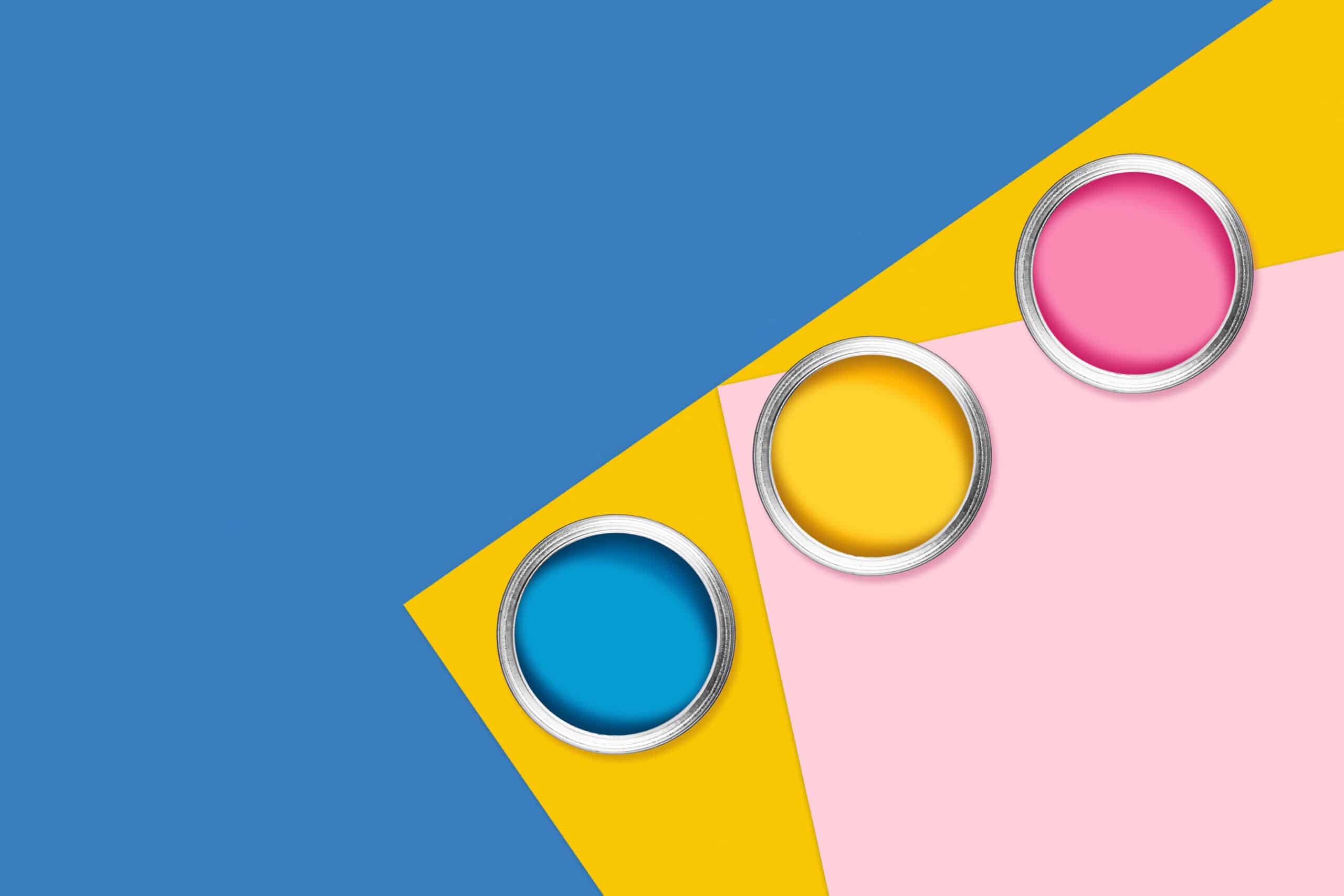 Blue, yellow and pink background with three cans of color paint, diagonal composition. Flat lay, top view, copy space.